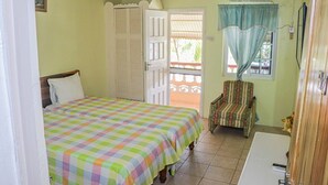 A bedroom with a bed, a chair, a window with curtains, and an air conditioning unit. - Columbus Inn (St. Ann's Bay)