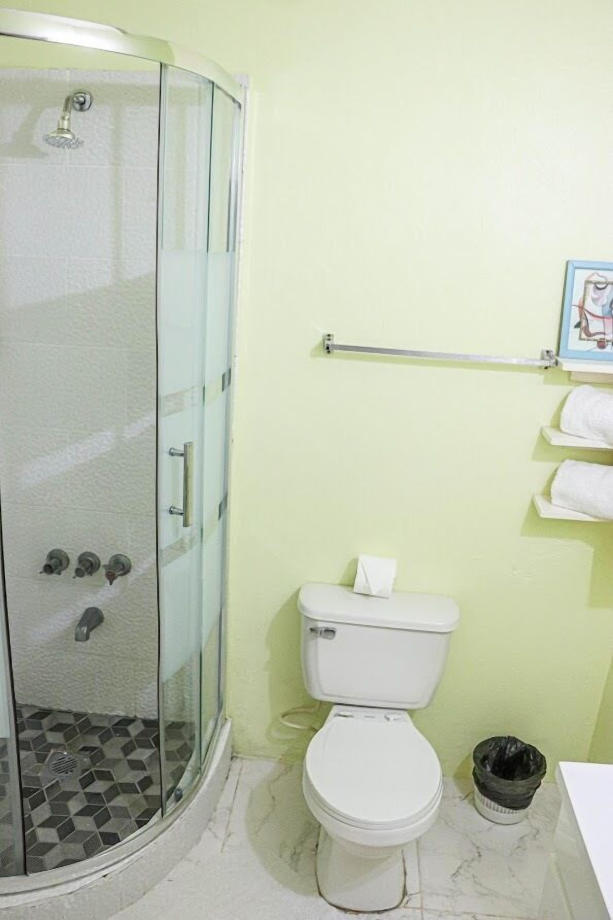 Un baño con ducha envuelta en vidrio, inodoro blanco, suelo de mármol y toallero con toallas.