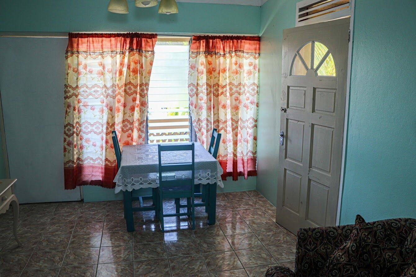A dining area with a table and chairs, a window with curtains, and a door.