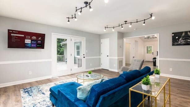A modern living room with a blue sofa, a glass coffee table, and a TV mounted on the wall. - Charlotte Pondside Oasis (Charlotte)