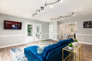 Een moderne woonkamer met een blauwe bank, een glazen salontafel en een aan de muur bevestigde televisie.