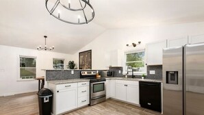 A modern kitchen with white cabinets, stainless steel appliances, and a black trash bin. - Charlotte Pondside Oasis (Charlotte)