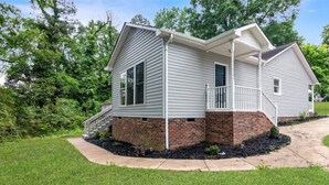 A single-story house with a brick foundation and white siding, a front porch, and a small front yard. - Charlotte Pondside Oasis (Charlotte)