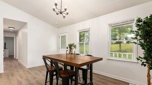 A dining area with a wooden table and black chairs, a chandelier, and a view of a tree through a window. - Charlotte Pondside Oasis (Charlotte)
