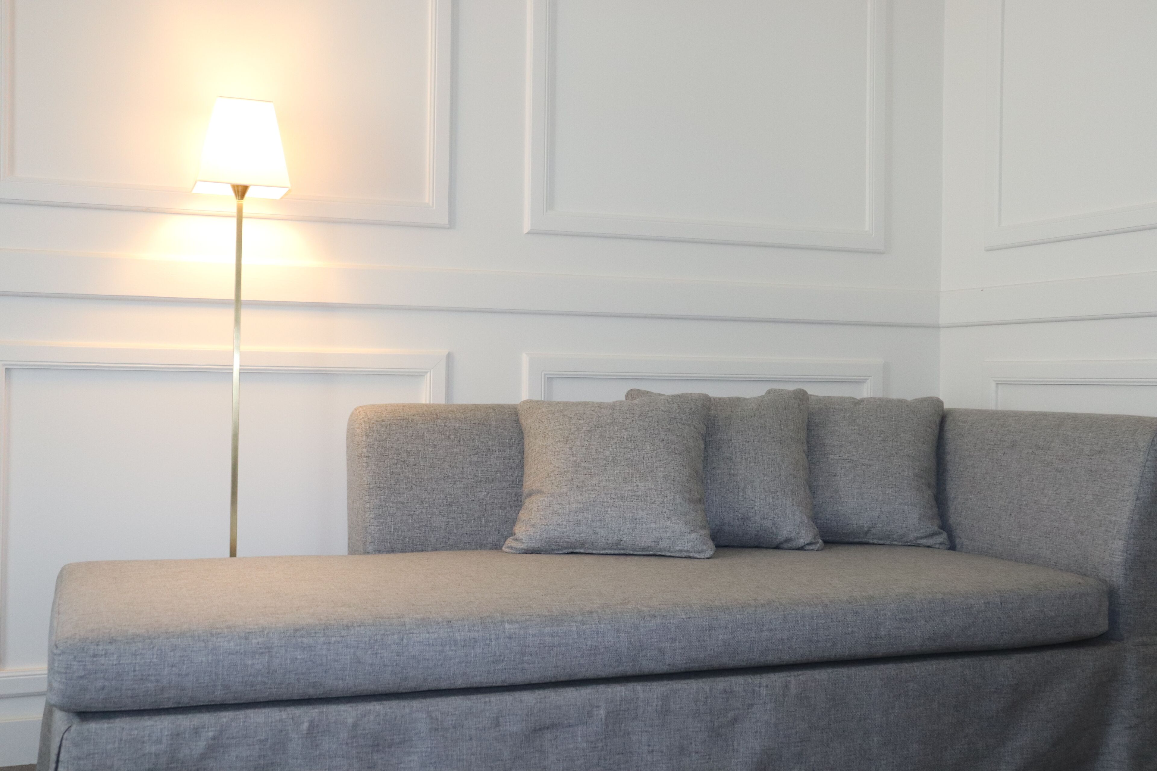 A neutral-toned sofa with a single lamp against a white paneled wall.