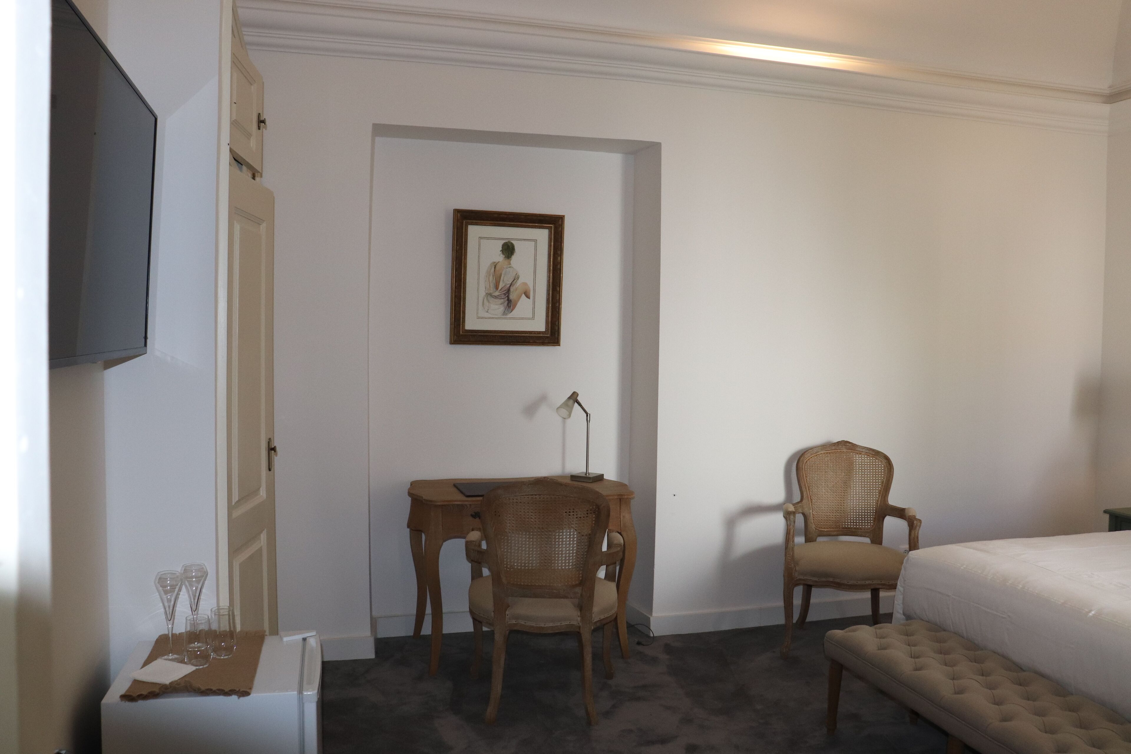 Habitación de hotel con cama, escritorio con silla, televisión y un cuadro en la pared.