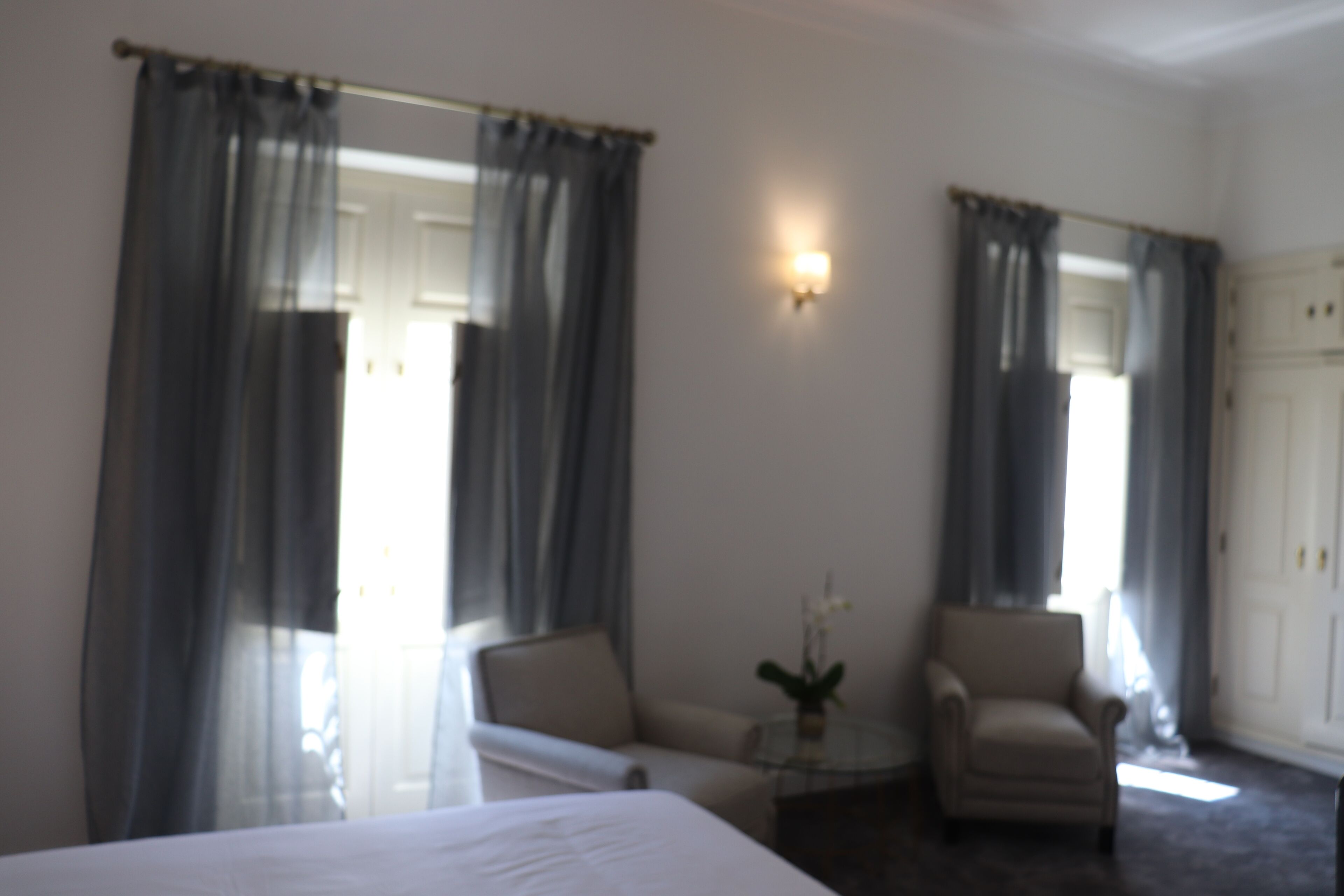 Ein Hotelzimmer mit einem Bett, zwei Sesseln, einem kleinen Tisch mit einer Vase und einer Tür.