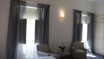 Ein Hotelzimmer mit einem Bett, zwei Sesseln, einem kleinen Tisch mit einer Vase und einer Tür.