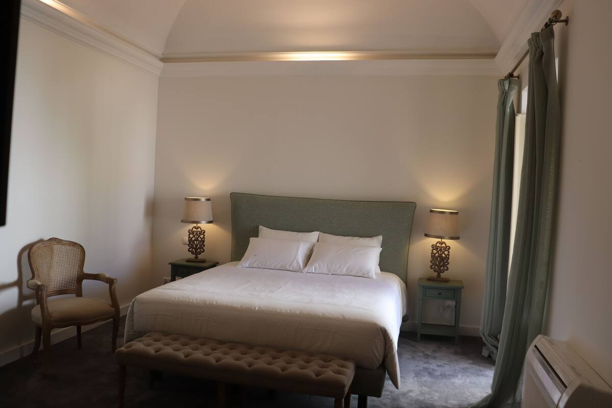 Une chambre à coucher bien aménagée, avec un grand lit, deux tables de chevet avec des lampes, une chaise et un banc.