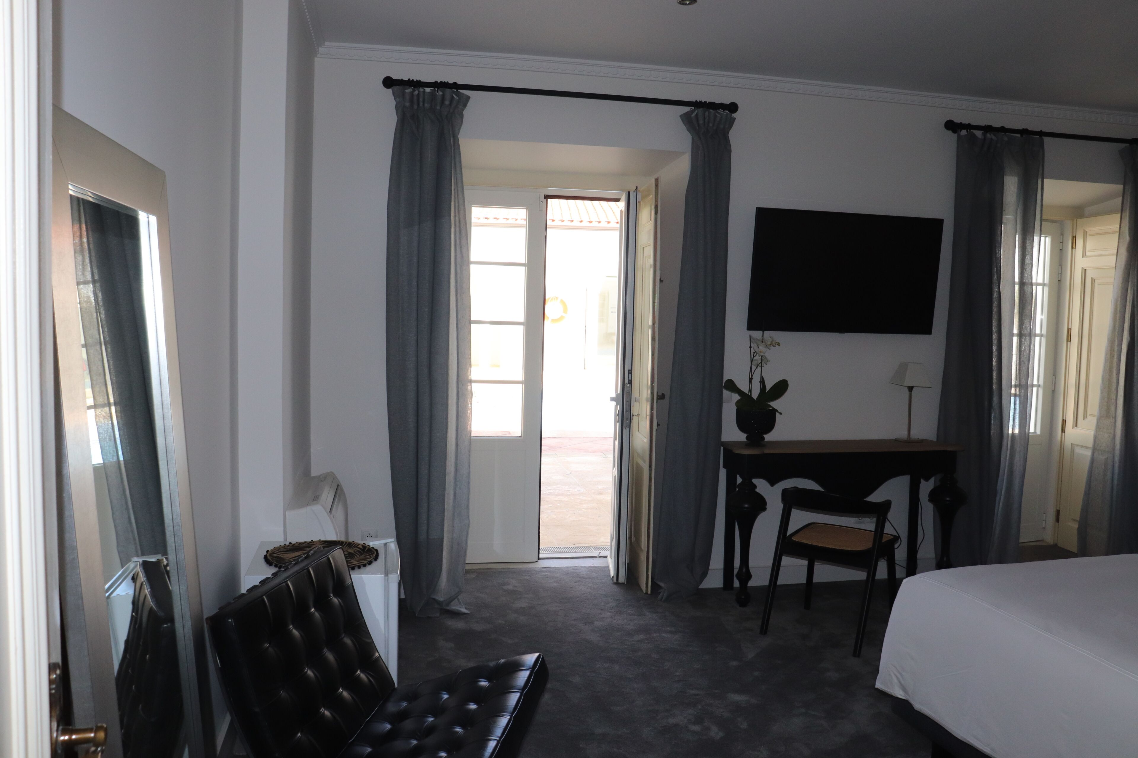 Quarto de hotel com cama, escrivaninha, cadeira e televisão.