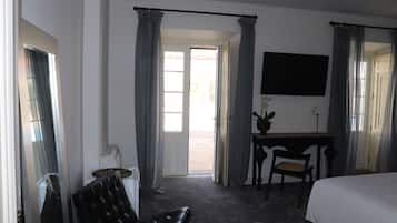 Quarto de hotel com cama, escrivaninha, cadeira e televisão.