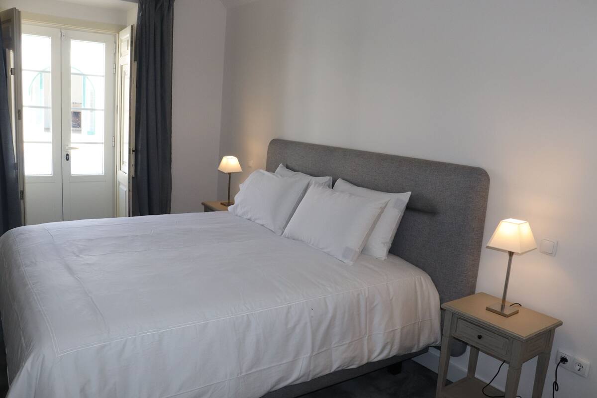 Un lit bien fait, avec du linge de lit blanc, deux tables de chevet avec des lampes et une porte avec des rideaux.