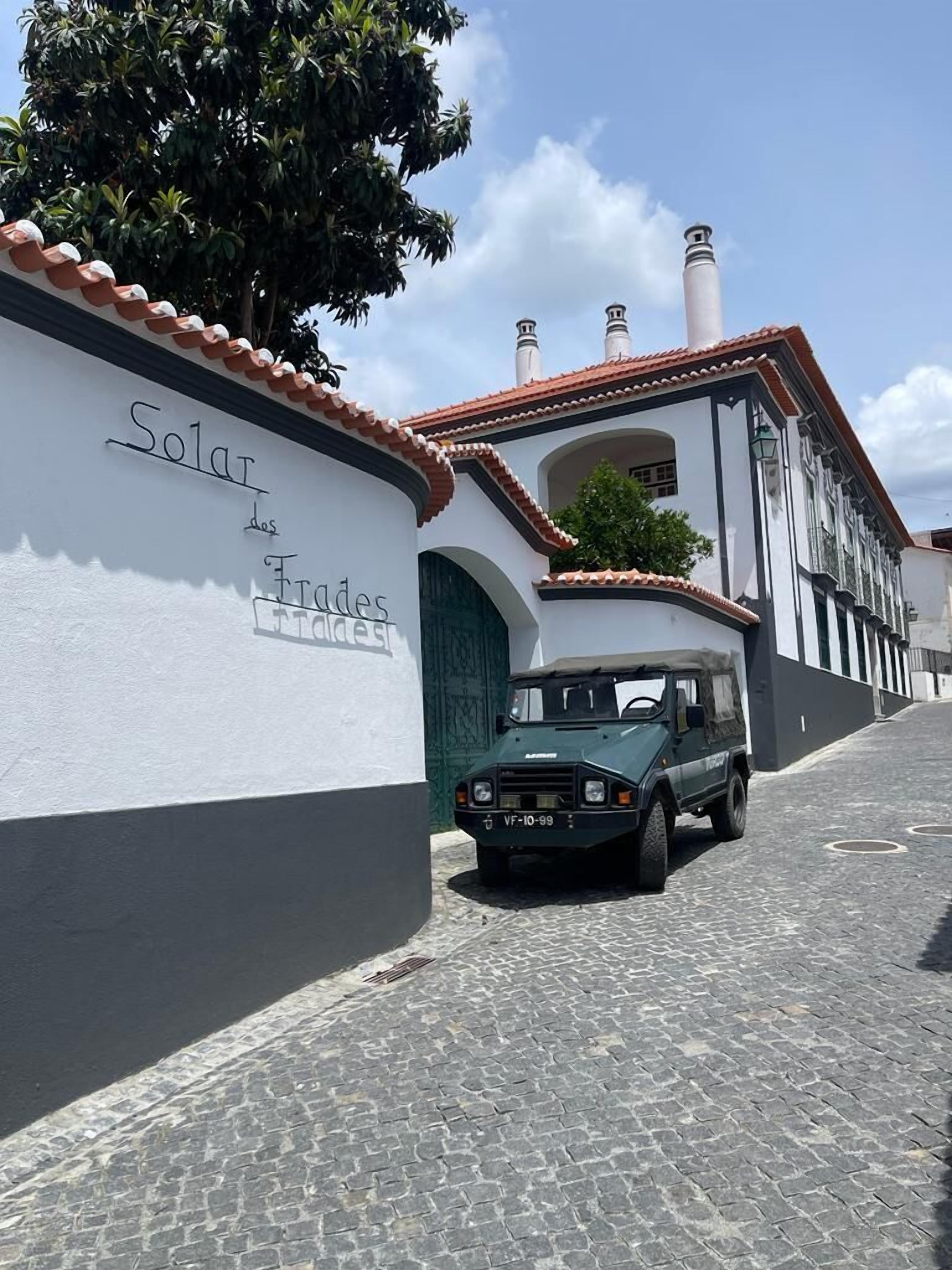 En bygning med et skilt, der siger "Solar des Forges", og en vintage, grøn bil parkeret foran.