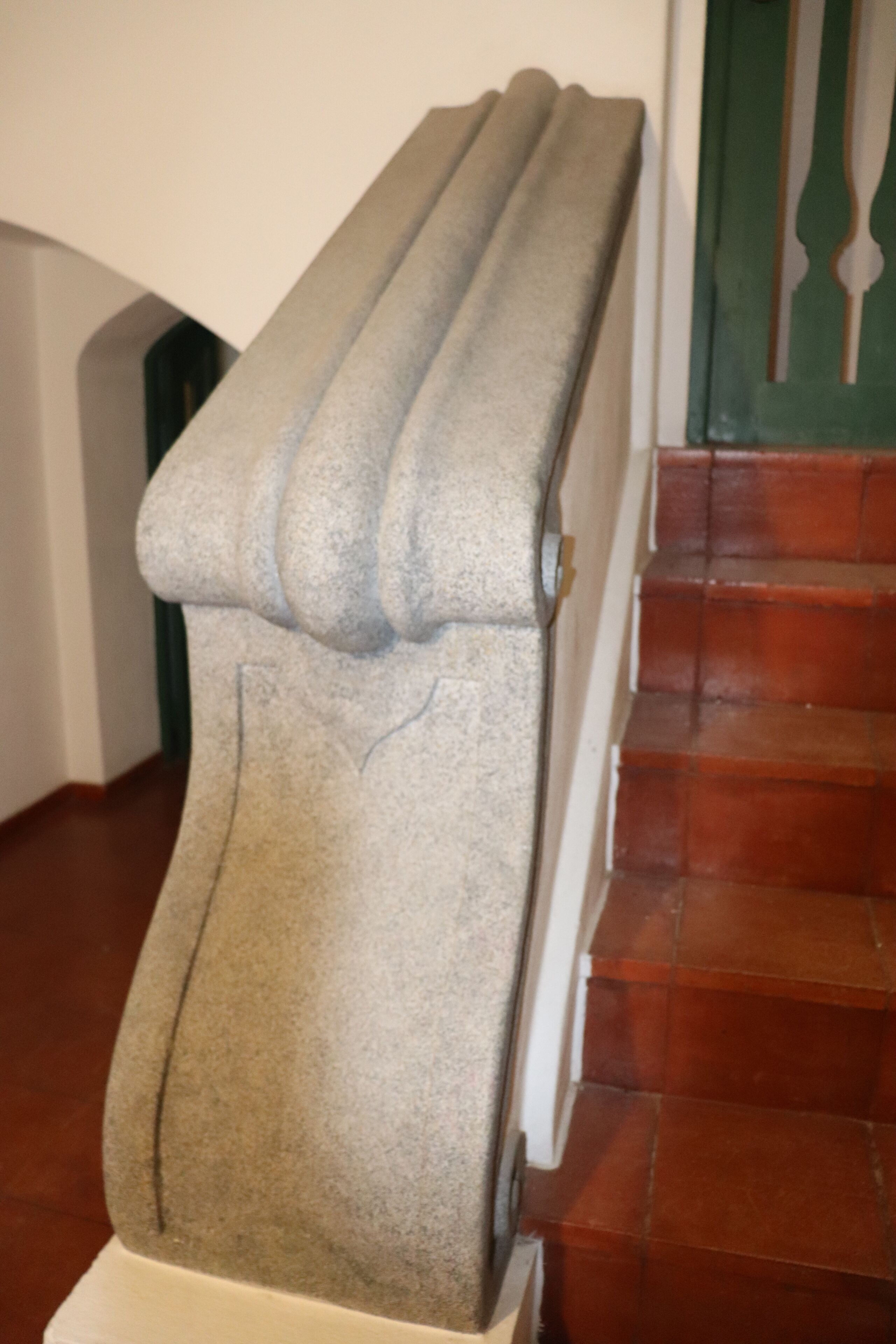 Una escalera con barandilla gris y texturizada, y peldaños rojos.
