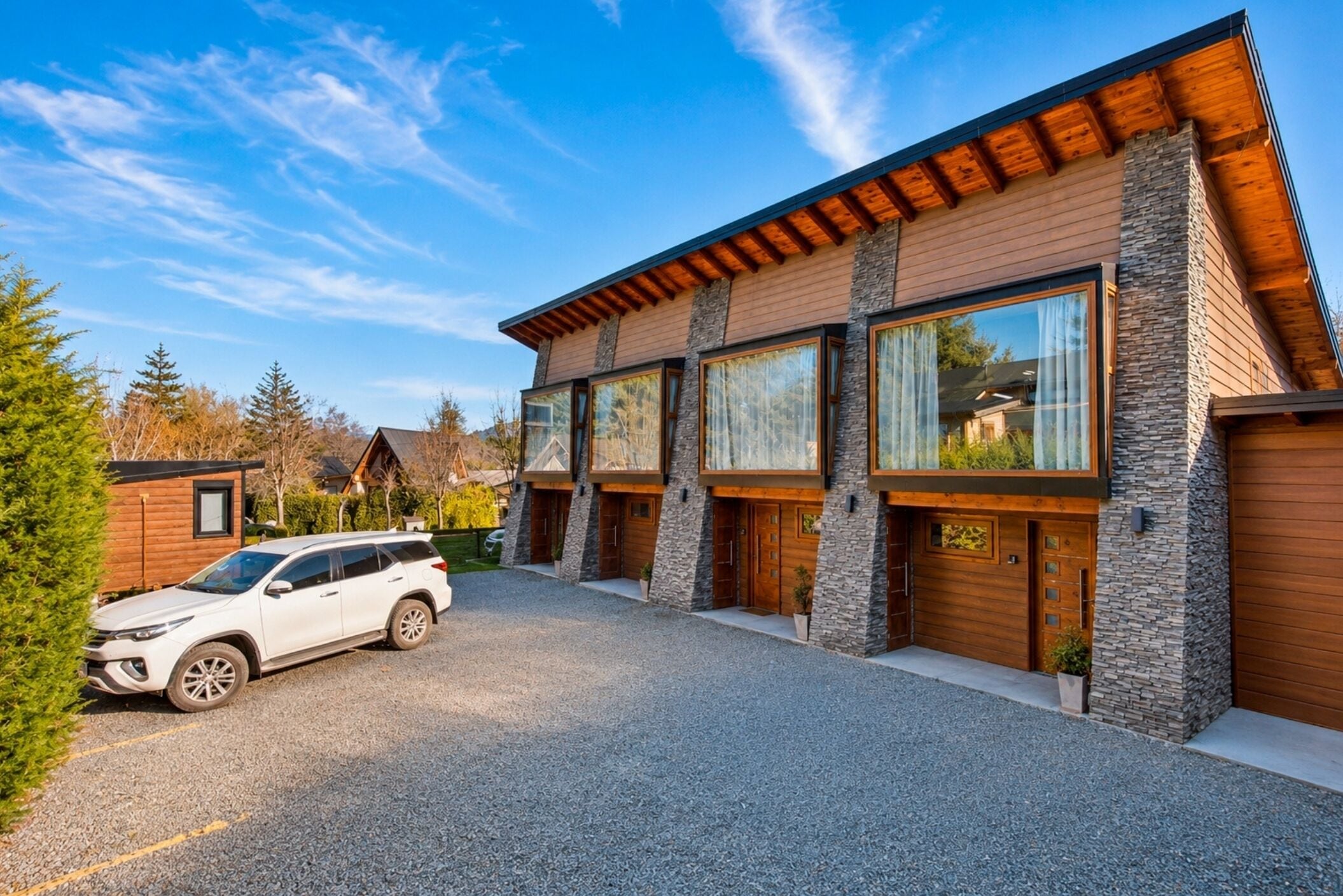 Una casa moderna de dos pisos con fachada de piedra, ventanas grandes y un coche estacionado adelante.