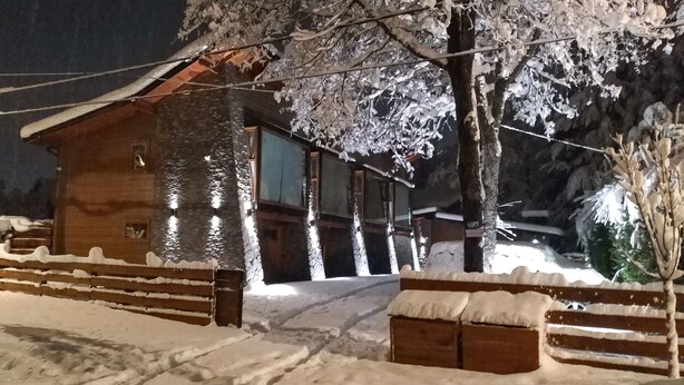 A wooden cabin with a snow-covered exterior, a visible window, and a wooden fence. - Los AMANCAYS (Villa La Angostura)