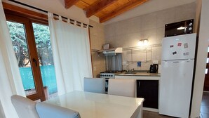 A kitchen with a white refrigerator, stove, and sink. There is a dining table with chairs. - Los AMANCAYS (Villa La Angostura)