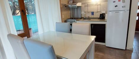 A kitchen with a white refrigerator, stove, and sink. There is a dining table with chairs.