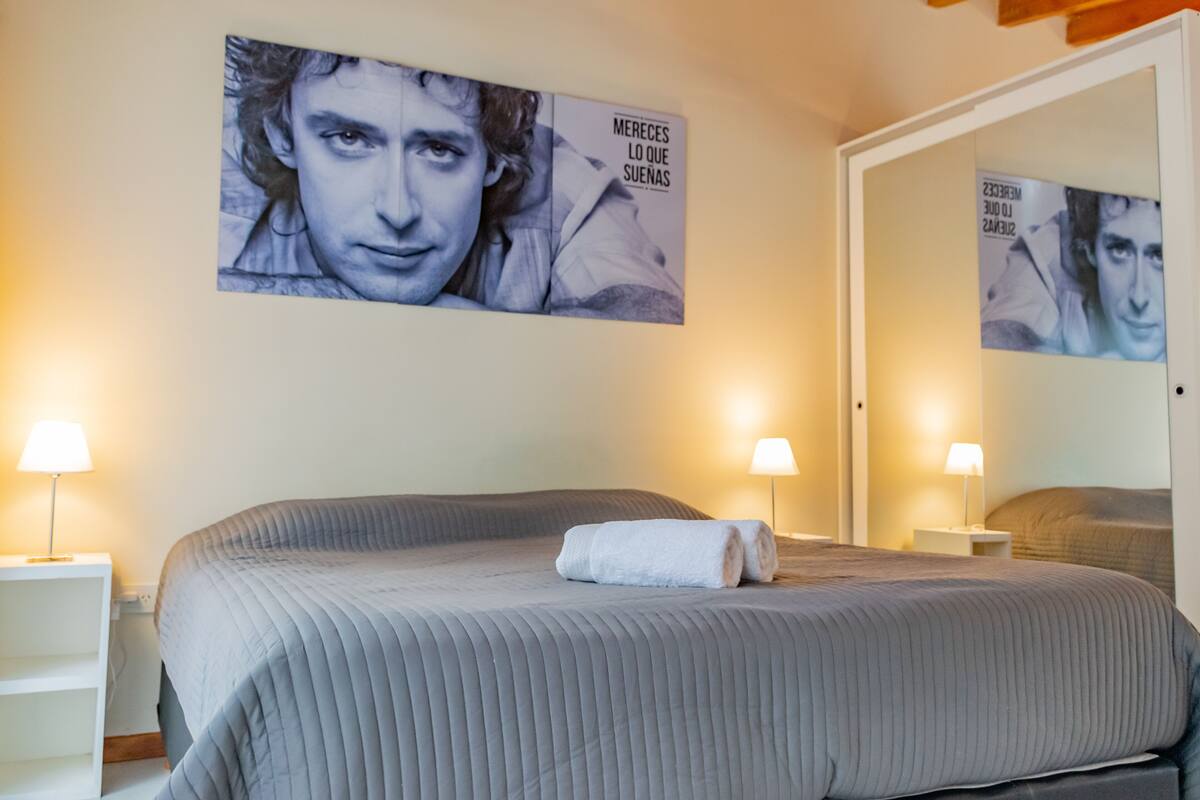 Une chambre d’hôtel avec un grand lit, deux lampes de chevet, une affiche au mur et un miroir.