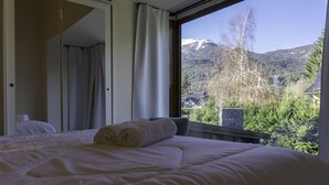 A bedroom with a large window, a bed with white linens, and a view of a mountainous landscape. - Los AMANCAYS (Villa La Angostura)