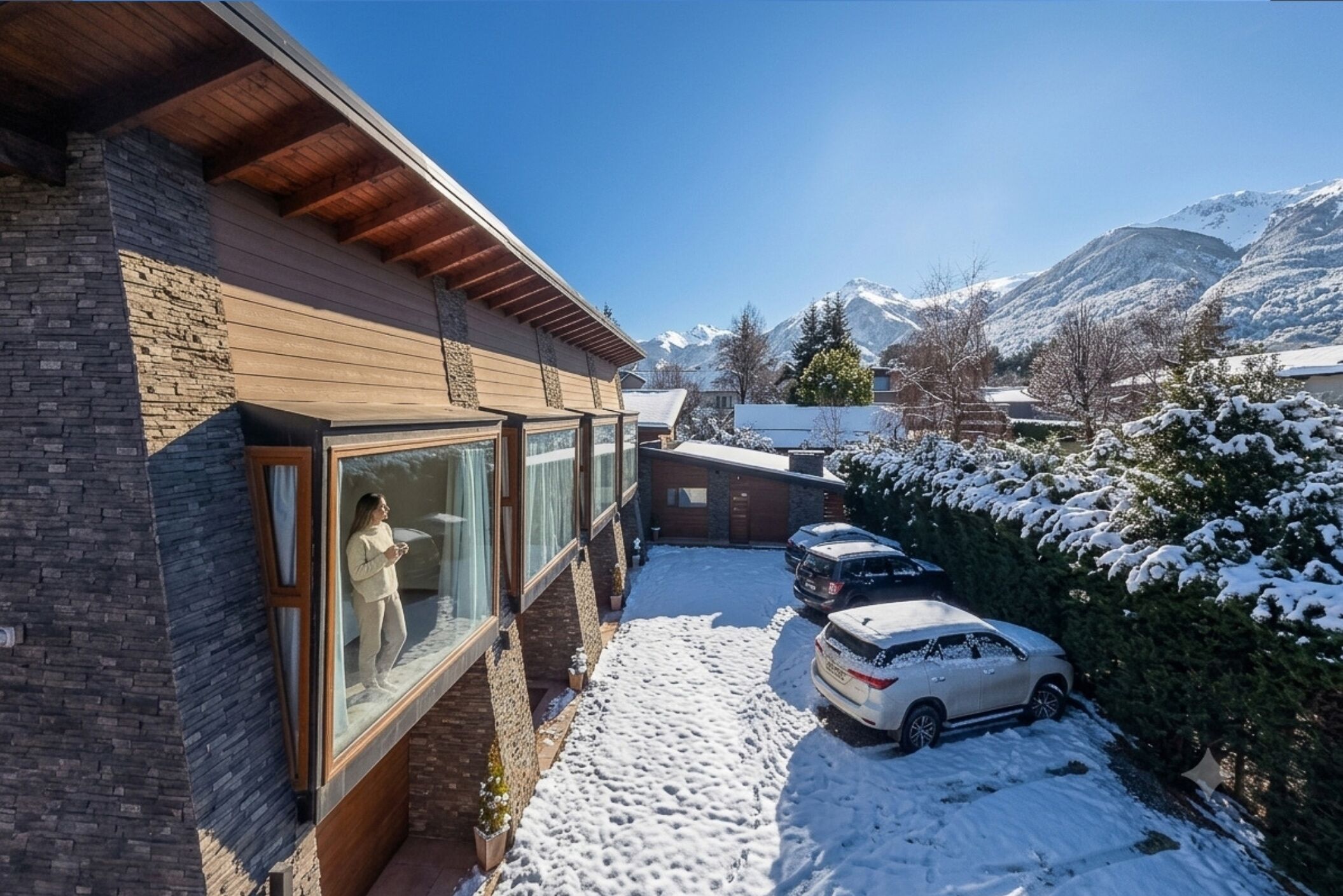 Un edificio residenziale con facciata in pietra, ampie finestre e vialetto coperto di neve.