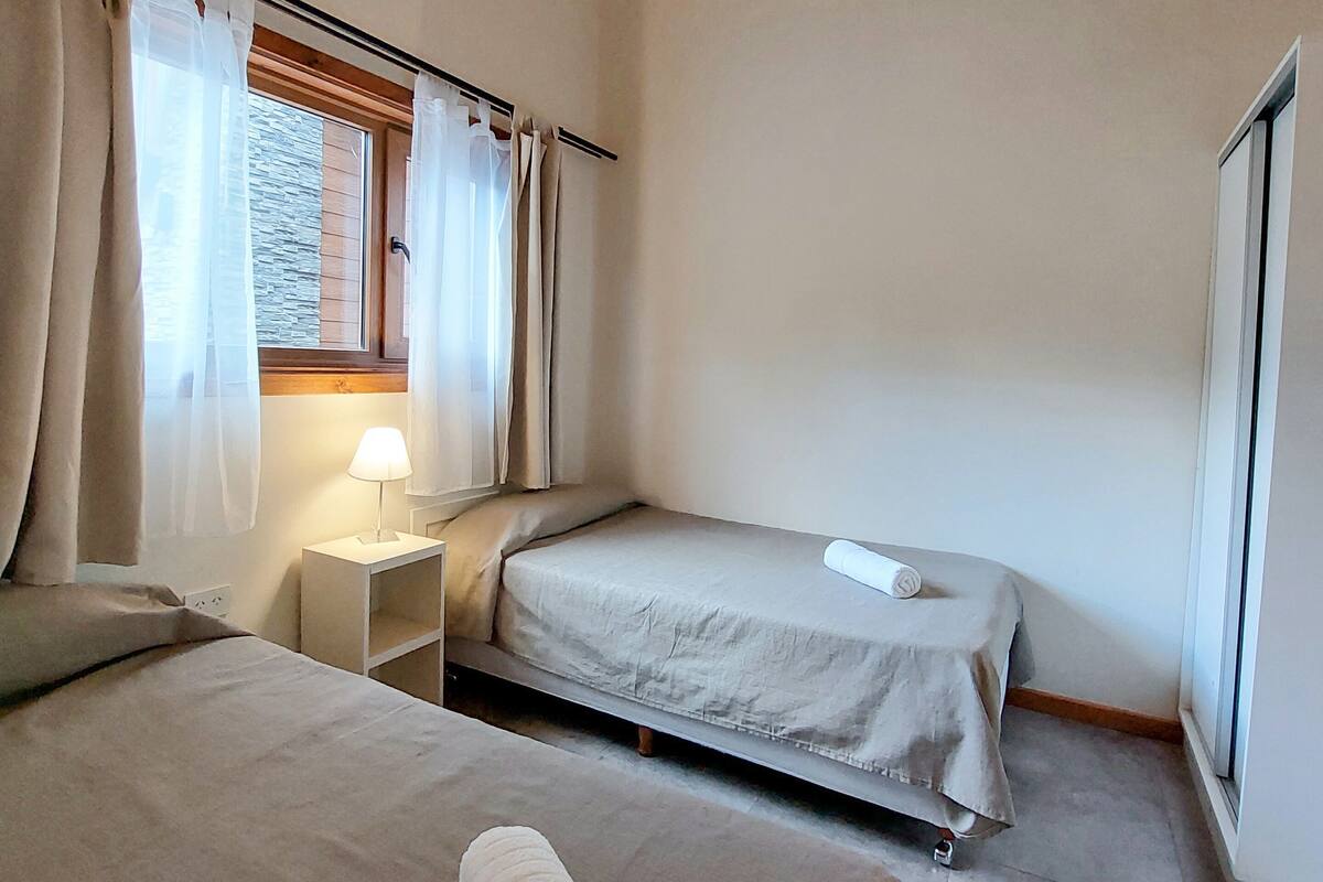 Une chambre avec deux lits, une fenêtre avec des rideaux, une lampe de chevet et un plafond en bois.