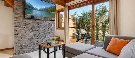 A modern living room with a stone wall, a wooden ceiling, a sofa, a table, and a view of a lake through a window.