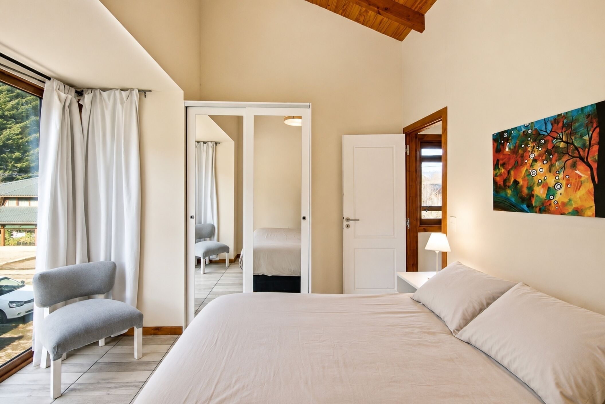 Un dormitorio con cama, una silla, una puerta que da a otra habitación y un cuadro en la pared.
