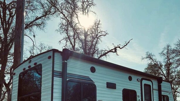 A white RV with the name 'CLIPPER' on the side, parked on a gravel surface with trees in the background. - Lake House (Beechgrove)