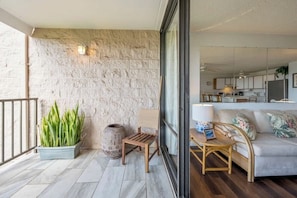 A balcony with a stone wall, a potted plant, a wooden chair, and a sofa with cushions.