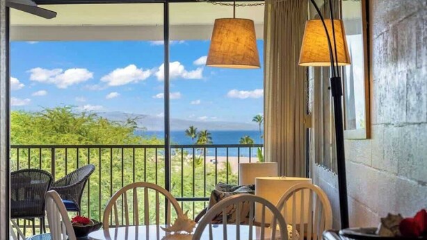 A balcony with a table and chairs, a view of the ocean, and a hanging lamp. - Ocean view 1 bedroom, AC, walk to shops, dining, & beaches (Kihei)