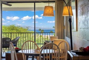 Un balcon avec une table et des chaises, une vue sur l’océan et une lampe suspendue.