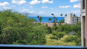 A view of a coastal area with buildings, palm trees, and a clear sky. - Ocean view 1 bedroom, AC, walk to shops, dining, & beaches (Kihei)