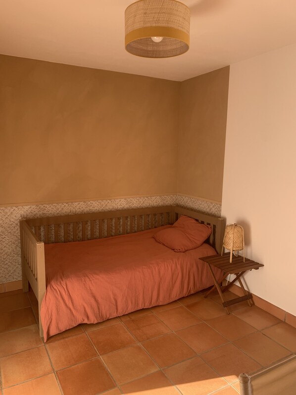 A small, cozy room with a single bed, a small table with a lamp, and a ceiling light fixture.