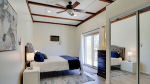 A bedroom with a bed, bedside tables, a ceiling fan, a large mirror, and a sliding glass door leading to a balcony. - California Vacation Rental with Hot Tub & Patio! (Yucca Valley)