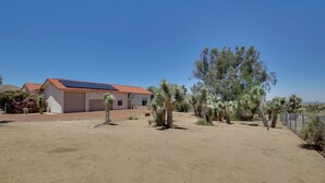 A house with a red roof, a garage, and a solar panel. There are several trees in the yard. - California Vacation Rental with Hot Tub & Patio! (Yucca Valley)