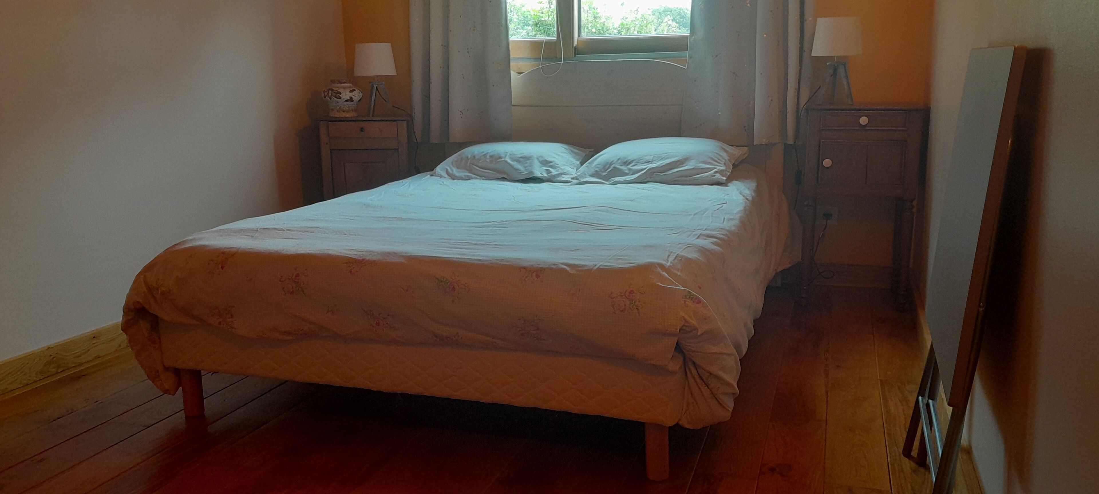 Une chambre à coucher avec un lit, un plancher en bois, des tables de chevet et une fenêtre avec des rideaux.