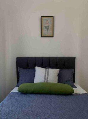 Una cama con cabecera oscura, varios almohadones y un almohadón verde.