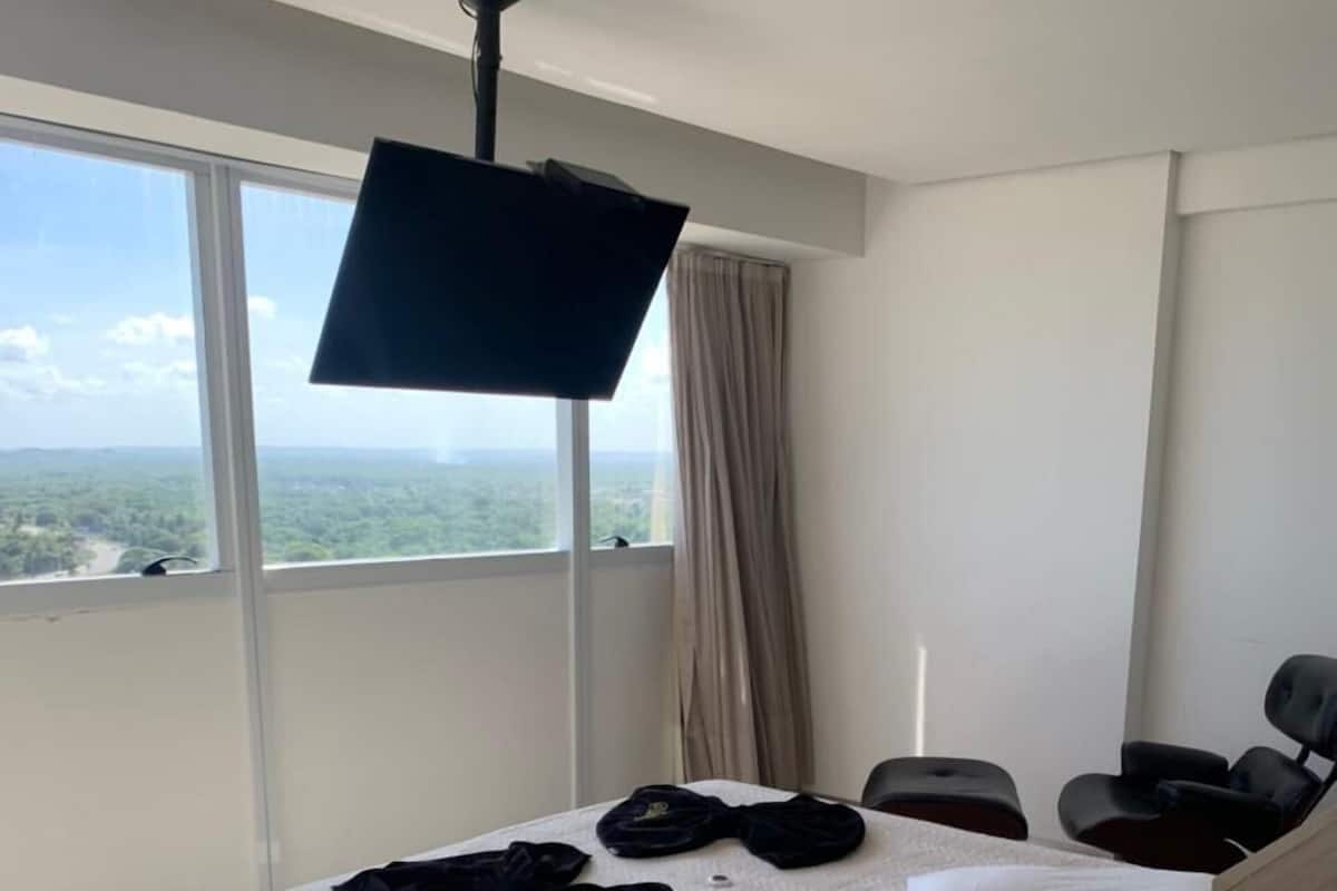 A modern hotel room with a large bed, a TV, a bedside table, and a view of a green landscape.