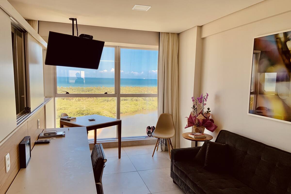 A modern living room with a large window, a flat-screen TV, a sofa, a small table, and a chair.