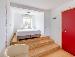 A bedroom with a bed, a window, a red door, and a staircase. - Pet-friendly Retreat (Heuvelland)