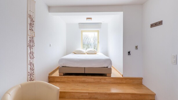 Une chambre avec un lit, une chaise et un escalier menant à une mezzanine.