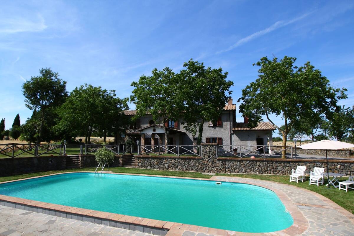 En swimmingpool med stentile, omgivet af en stenvæg og en græsplæne.