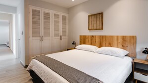 A bedroom with a large bed, wooden headboard, white walls, and a wooden floor. - Casa Love 3B (Panama City)