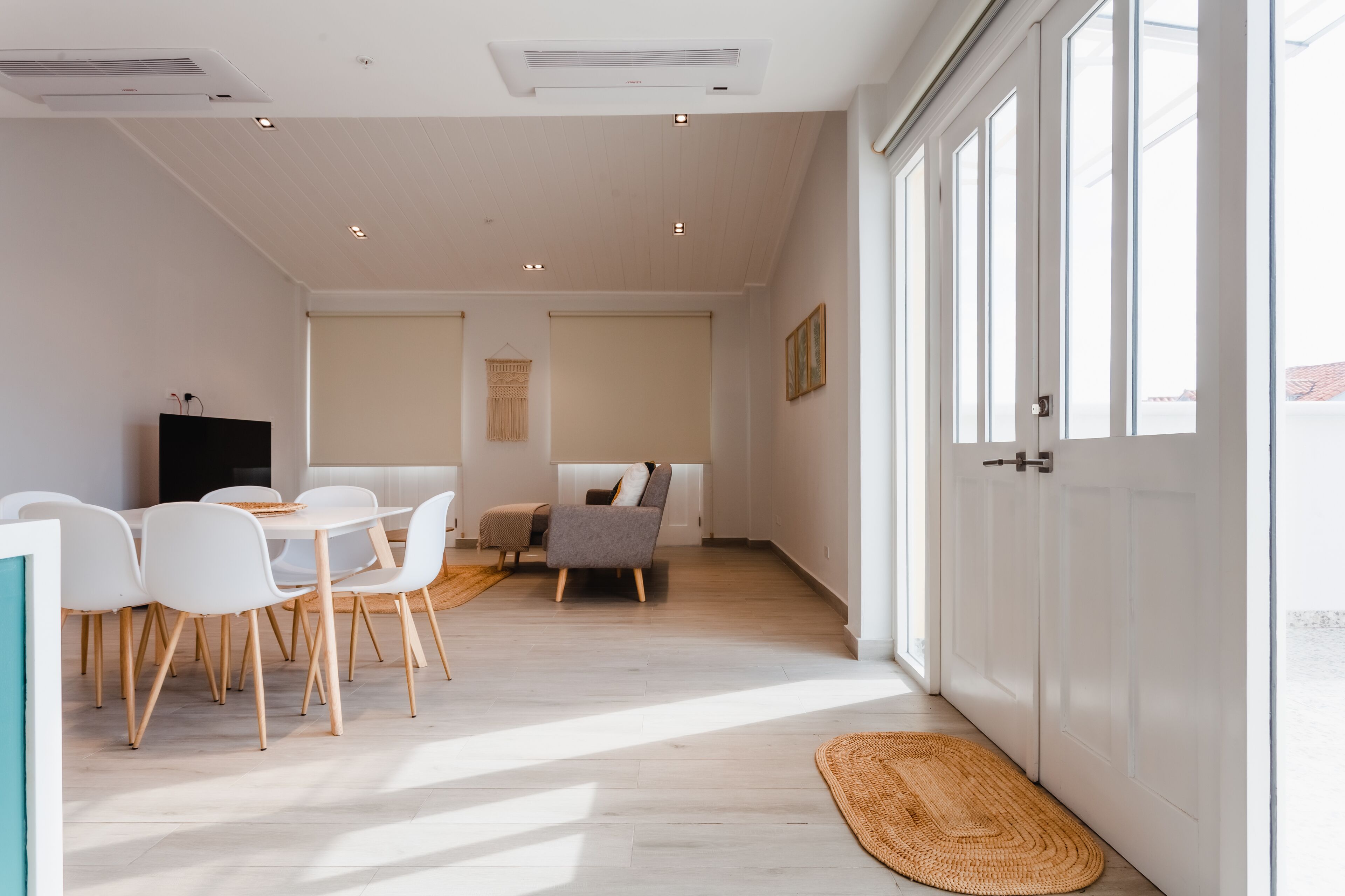 A modern, well-lit room with a dining area, a sofa, and a television.