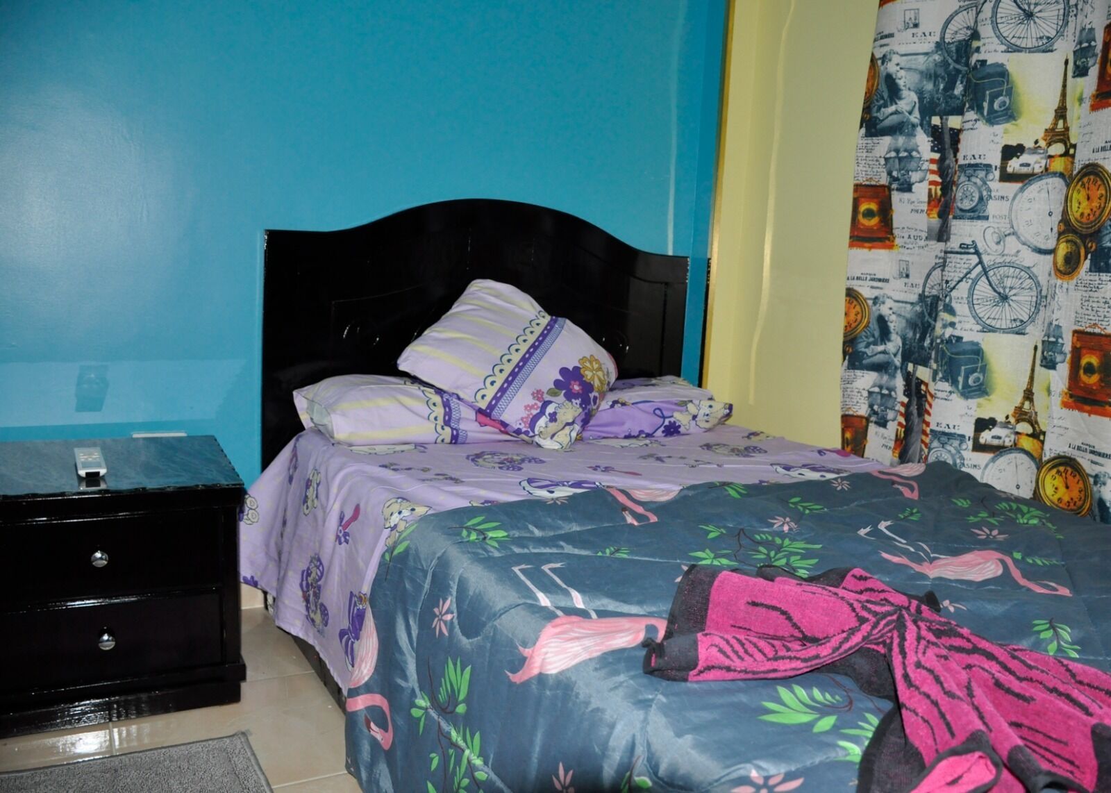 A bedroom with a bed, pillows, a nightstand, and a wall with a patterned tapestry.