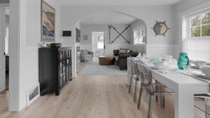 Une cuisine spacieuse avec un coin repas, comprenant une table blanche, des chaises transparentes et une grande fenêtre.