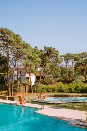 A swimming pool with a clear view of a building in the background, surrounded by trees and greenery. - Parque do Rio Ofir Hotel (Esposende)