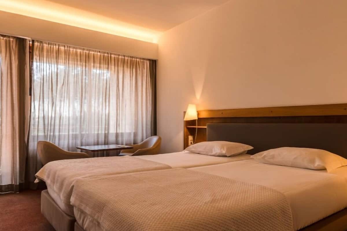 A hotel room with a large bed, a chair, a small table, and a lamp.