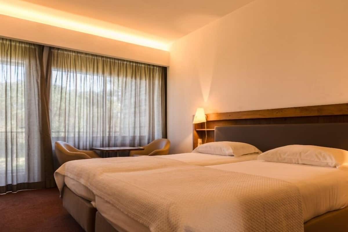 A hotel room with a large bed, a chair, a table, and a window with curtains.